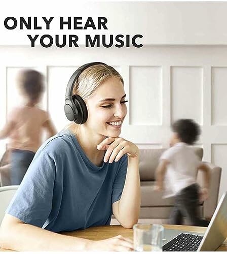 Woman wearing headphones smiling at laptop with kids playing in the background.