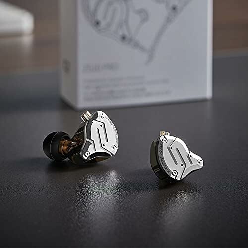 Sleek metallic earbuds displayed on a table with packaging in the background.